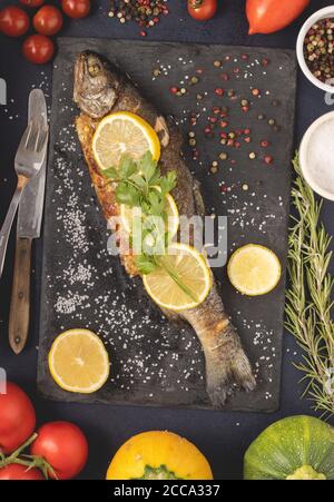 Gegrillte Forelle mit Olivenöl, Petersilie, Pfeffer, Salz und Zitrone auf den dunklen Hintergrund gelegt. Gesunde mediterrane Küche und Diät-Konzept, Draufsicht. Stockfoto