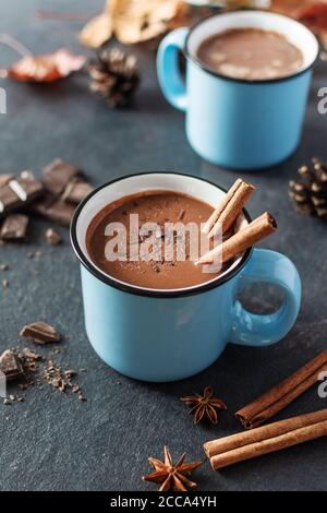 Würzige heiße Schokolade mit Zimt und Sternanis in emaillblauen Tassen auf schwarzem Hintergrund. Getränke bei kaltem Herbstwetter. Stockfoto