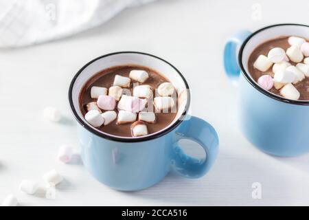 Heiße Schokolade mit Marshmallows in einem blauen emaillierten Becher auf weißem Tisch. Heißer gemütlicher Drink für Herbst oder Winter. Stockfoto