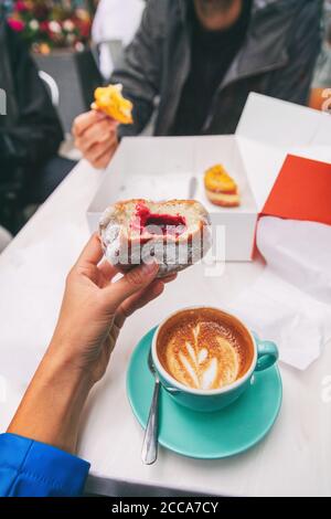 Essen Selfie Mädchen essen eine Beere gefüllt berliner Donut beim Trinken einer Cappuccino Kaffeetasse im Café . Stadt städtischen Touristen reisen Lifestyle, POV Stockfoto