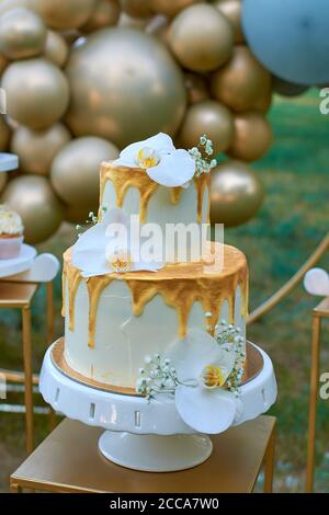 Eine zweistöckige Hochzeitstorte mit orchedea Blumen geschmückt. Hochzeitsdekoration in Goldfarbe, Ballon-Dekor. Stockfoto