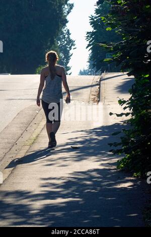 Silhouette einer jungen Frau in Laufausrüstung, die mit einem Mobiltelefon bergauf geht. Stock Foto. Stockfoto