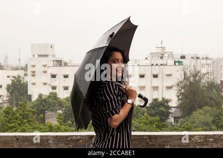 Indische Frau mit Regenschirm im Regen. Blick in die Kamera. Stockfoto