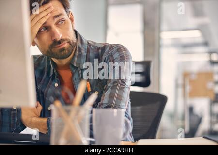 Müde junger Mann sitzt am Tisch im Büro Stockfoto