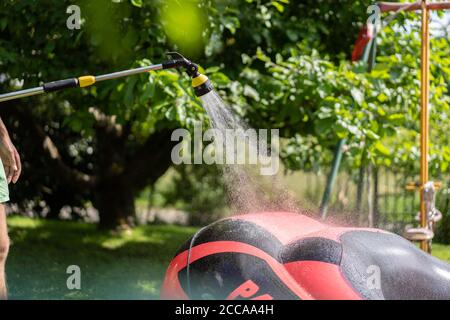 Aufräumen von rot aufgeblasenen Gummiboot durch jungen Mann. Nahaufnahme auf grünem Gras an sonnigen Tagen. Stockfoto