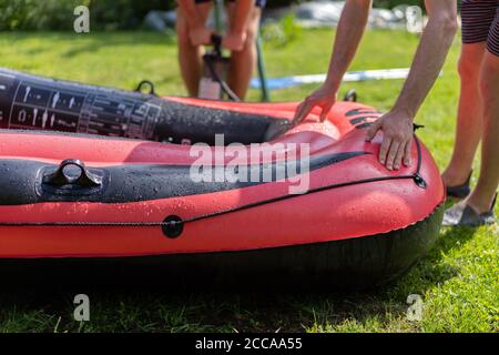 Rotes Gummiboot wird mit einer Handpumpe aufgepumpt und von zwei jungen Männern kontrolliert. Nahaufnahme auf grünem Gras an sonnigen Tagen. Stockfoto