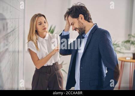 Bärtiger Mann mit Kopfschmerzen während der Arbeit mit Dame im Büro Stockfoto