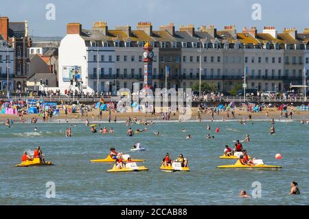 Weymouth, Dorset, Großbritannien. August 2020. Wetter in Großbritannien. Urlauber genießen eine Fahrt auf Pedalos auf dem Meer mit dem vollen Strand hinter ihnen im Badeort Weymouth in Dorset an einem windigen Tag mit sengenden heißen Sonnenschein und klaren blauen Himmel. Bild: Graham Hunt/Alamy Live News Stockfoto