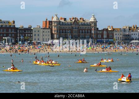 Weymouth, Dorset, Großbritannien. August 2020. Wetter in Großbritannien. Urlauber genießen eine Fahrt auf Pedalos auf dem Meer mit dem vollen Strand hinter ihnen im Badeort Weymouth in Dorset an einem windigen Tag mit sengenden heißen Sonnenschein und klaren blauen Himmel. Bild: Graham Hunt/Alamy Live News Stockfoto