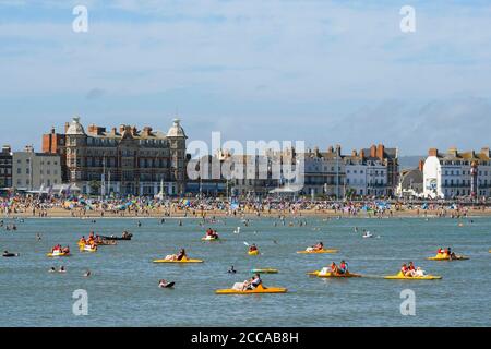 Weymouth, Dorset, Großbritannien. August 2020. Wetter in Großbritannien. Urlauber genießen eine Fahrt auf Pedalos auf dem Meer mit dem vollen Strand hinter ihnen im Badeort Weymouth in Dorset an einem windigen Tag mit sengenden heißen Sonnenschein und klaren blauen Himmel. Bild: Graham Hunt/Alamy Live News Stockfoto