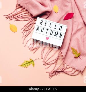 Leuchtkasten mit Hello Autumn Text auf pastellfarbenem Hintergrund. Kuscheliger drapierter Schal und Blätter. Stockfoto