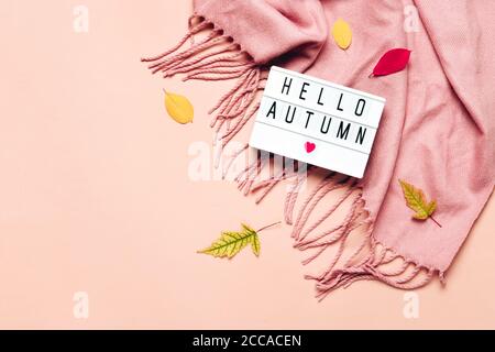 Leuchtkasten mit Hello Autumn Text auf pastellfarbenem Hintergrund. Kuscheliger drapierter Schal und Blätter. Stockfoto