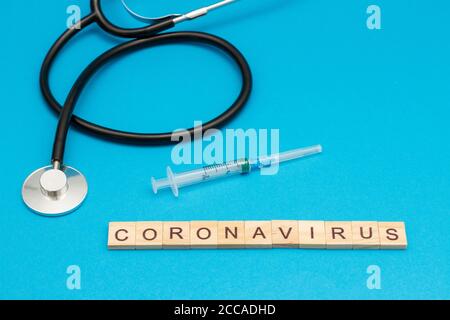 Word CORONAVIRUS aus Holzwürfeln auf blau mit Stethoskop Und chirurgische Spritze Stockfoto