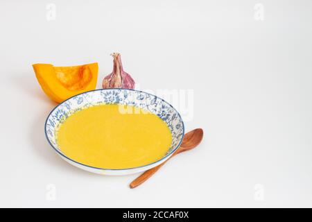 Kürbiscremesuppe in Schüssel auf weißem Hintergrund. Speicherplatz kopieren. Eine Scheibe Kürbis, Knoblauch und einen Holzlöffel auf dem Tisch Stockfoto