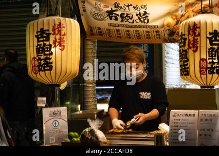 TAICHUNG CITY, TAIWAN - 14. Januar 2020: Ein Chinese serviert Grillgerichte auf dem Feng Chia Nachtmarkt in Taichung City in Taiwan - Januar 2020. Stockfoto