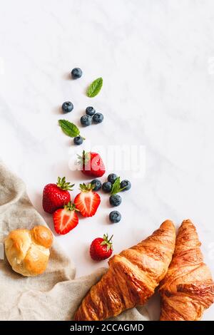 Sommer Frühstück. Erdbeeren, Heidelbeeren, Croissants und eine Pariser Brioche auf weißem Marmorboden. Stockfoto