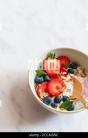 Sommer Frühstück. Schüssel Joghurt mit Erdbeeren, Heidelbeeren und Müsli auf weißem Marmorboden. Stockfoto