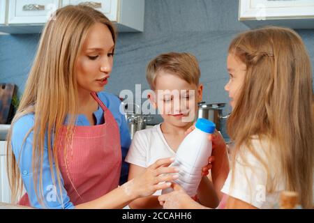 Cute blonde Kinder helfen ihre Mutter in der Küche vorbei Flasche Milch Stockfoto