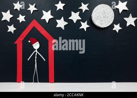 Stick Mann Figur trägt santa Hut allein in einem roten Haus. Isolation und zu Hause bleiben Konzept während covid Weihnachten. Stockfoto