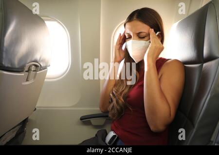 COVID-19 Junge Frau mit KN95 FFP2 Maske fühlt sich im Flugzeug unwohl. Angst vor fliegender Frau im Flugzeug. Stress, Kopfschmerzen, Reisekrankheit und Luftkrankheit Stockfoto