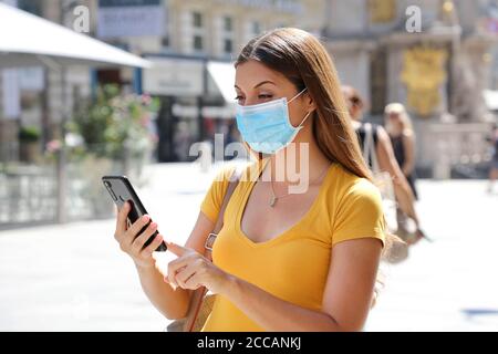 COVID-19 optimistische junge Frau mit Schutzmaske lesen gute Nachrichten Auf dem Mobiltelefon Stockfoto