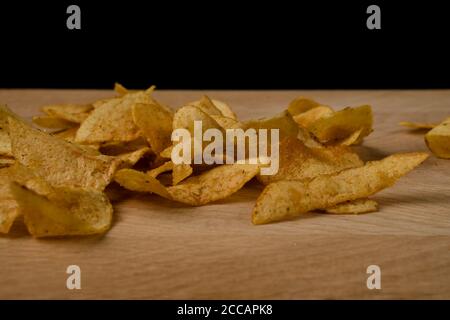 Appetitliche Kartoffelchips sind auf einem Holzbrett verstreut Stockfoto