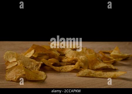 Appetitliche Kartoffelchips sind auf einem Holzbrett verstreut Stockfoto