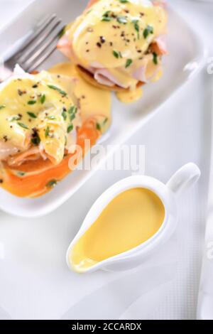 Hollandaise Butter Sauce in einem Soße Boot zum Frühstück mit Eiern Benedict serviert - gebratenes englisches Brötchen, Schinken, pochierte Eier, Stockfoto