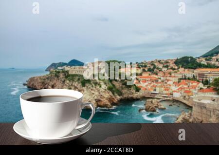 Tasse schwarzen Kaffee vor dem Blick auf blaues Meer und felsigen Küste Hintergrund. Dubrovnik Altstadt von alten Mauern umgeben. Blick von oben auf die roten Dächer Stockfoto