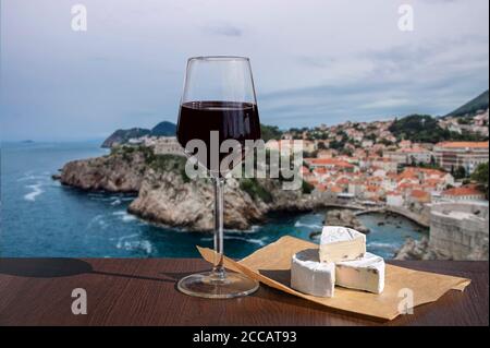 Ein Glas Wein mit Brie-Käse vor dem Blick auf das blaue Meer und felsigen Küste Hintergrund. Dubrovnik Altstadt von alten Mauern umgeben. Blick von oben Stockfoto