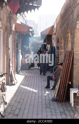 Essaouira, Marokko - 16. März 2018: Eine schmale Straße in Essaouira zwischen Sonne und Schatten mit Marokkanern flanieren geteilt Stockfoto