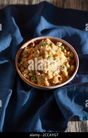 Südindisches Frühstück vegan herzhaftes Gemüse Grießbrei Rava UPMA auf blauem Textil-Hintergrund. Authentisches vegetarisches Essen Stillleben. Stockfoto