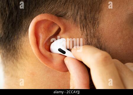 Izmir, Türkei - 7. August 2020: Nahaufnahme von weißen Apple AirPods auf dem Ohr eines Mannes. Halten Sie ihn mit einer Hand und drücken Sie die Taste. Stockfoto