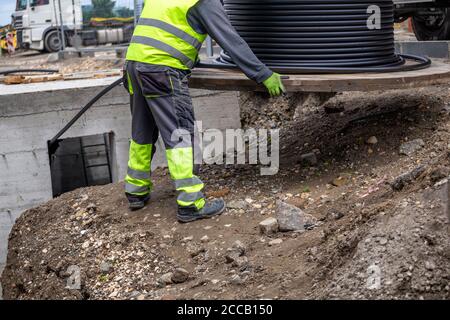 Arbeiter rollt schwarzes Kabel mit Holzspule ab. Verlegen des Netzkabels unter den Boden. Stockfoto