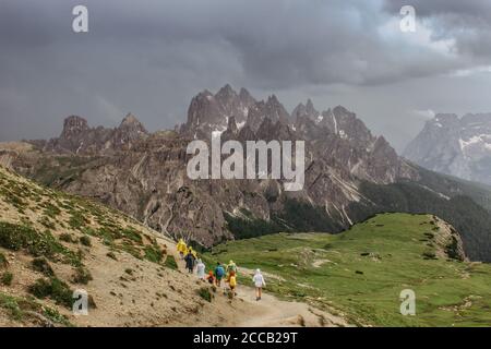 Menschen in Regenmäntel Wandern in den Dolomiten, Italien.Regentag im Freien. Blick auf die Berglandschaft mit dunklen launischen Sturmwolken.dramatische Wolken über Gipfeln o Stockfoto