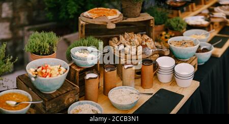 Kupferbecher, Teller und Pizza- und Pappbretter auf einem langen Tisch mit Küchenutensilien. Buffettisch zum Frühstück im Restaurant. Stockfoto