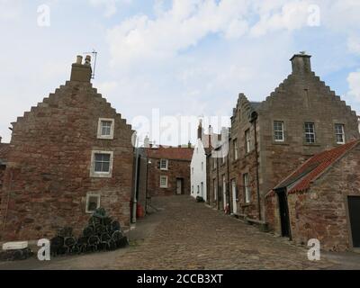 Enge gepflasterte Straßen mit den traditionellen abgestuften Giebeln von Fischerhütten und Häusern auf einer steilen Straße, die zum Hafen von Crail führt. Stockfoto