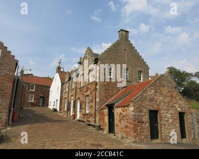 Enge gepflasterte Straßen mit den traditionellen abgestuften Giebeln von Fischerhütten und Häusern auf einer steilen Straße, die zum Hafen von Crail führt. Stockfoto