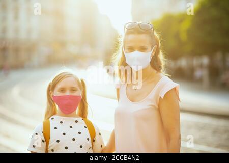 Leben während der covid-19 Pandemie. Portrait von eleganten Mutter und Kind mit Masken und gelben Rucksack immer bereit für die Schule draußen. Stockfoto