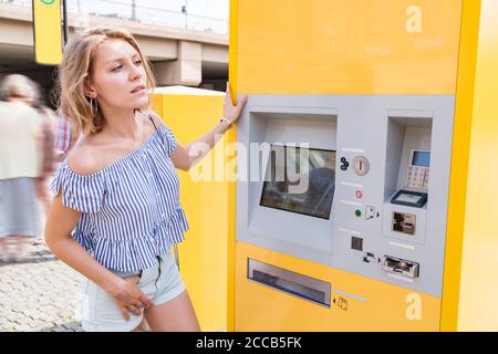 Junge blonde Frau kauft Tickets an einem Ticketautomaten Straßenbahnhaltestelle Stockfoto