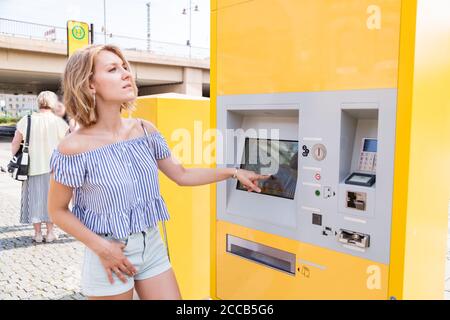 Junge blonde Frau kauft Tickets an einem Ticketautomaten Straßenbahnhaltestelle Stockfoto