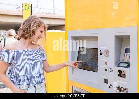 Junge blonde Frau kauft Tickets an einem Ticketautomaten Straßenbahnhaltestelle Stockfoto