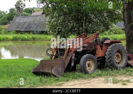 Traktor mit roter Farbe, sehr alt, aber immer noch in Gebrauch, geparkt neben einem See. Stockfoto