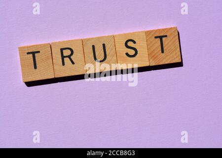 Vertrauen, Wort in hölzernen Buchstaben auf violettem Hintergrund isoliert Stockfoto