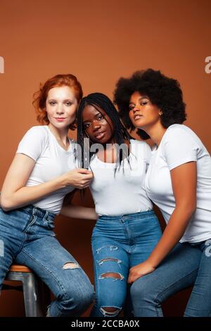Junge hübsche kaukasische, afro, skandinavische Frau posiert fröhlich zusammen auf braunem Hintergrund, Lifestyle diverse Nationalität Menschen Konzept Stockfoto