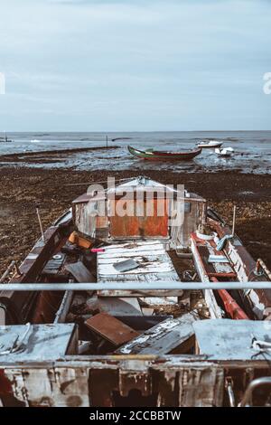 Vertikale Weitwinkel-Ansicht eines alten einsamen Fischerboot mit einer Kabine voller alter Dinge und Müll an einem flachen Ufer, mit anderen Booten vertäut Stockfoto