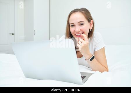 Ein Mädchen lächelt und benutzt ihren Laptop auf dem liegend Bett Stockfoto