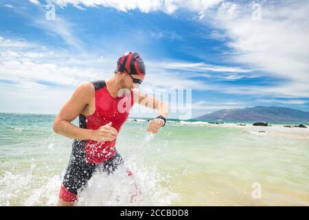 Smartwatch Triathlon Schwimmen Sport Mann Abschluss schwimmen Überprüfung der Herzfrequenz auf Smart-Uhr. Männliche Triathlet Schwimmer läuft aus dem Meer. Professionell Stockfoto