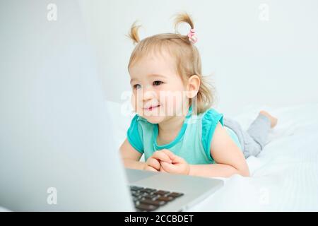 Glückliches Kleinkind liegt auf dem Bett und schaut auf die Notebook Stockfoto