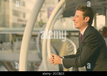 Profil anzeigen von Happy Geschäftsmann, lächeln und Denken in der Fußgängerbrücke in Bangkok City Stockfoto